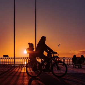 Photographie d'art de 2 silhouettes à vélo racontant l'histoire d'un père et sa fille se baladant au bord du bassin au soleil couchant.