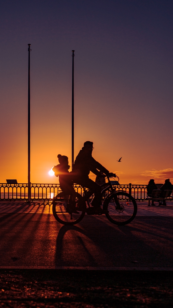 Photographie d'art de 2 silhouettes à vélo racontant l'histoire d'un père et sa fille se baladant au bord du bassin au soleil couchant.
