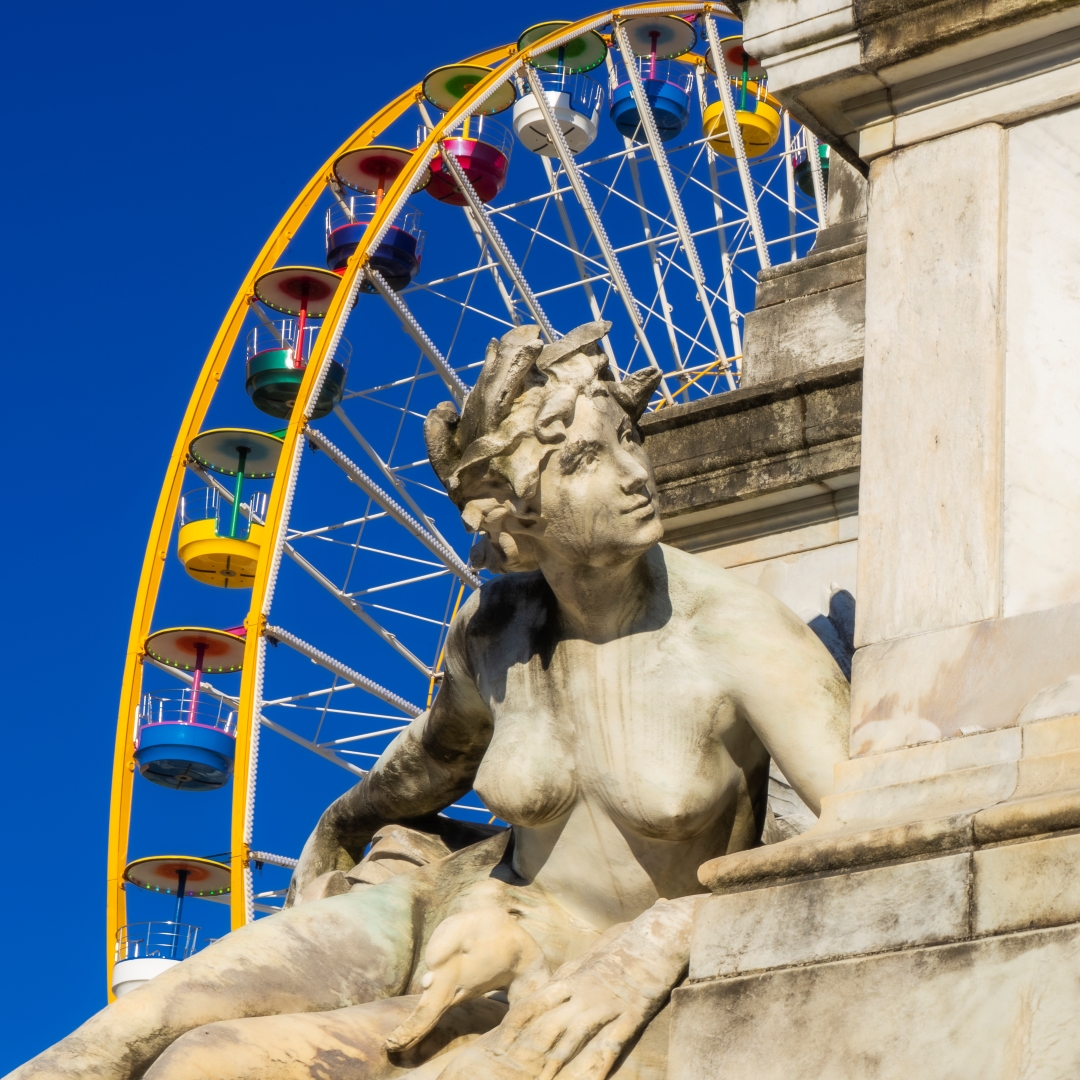 La Garonne apprêtée. Photographie originale par Anne-Laure Boisseau. Statue de la Garonne à Bordeaux avec grande roue colorée de la fête foraine en arrière-plan – monument aux Girondins, ciel bleu.