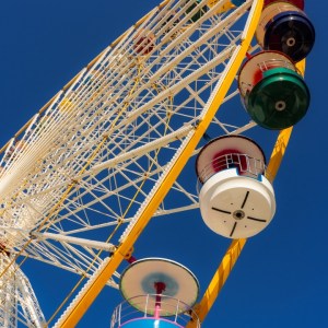 Grande roue colorée de la Foire aux Plaisirs à Bordeaux vue en contre-plongée – ciel bleu, cabines multicolores, photographie d’art contemporaine.