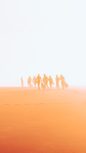 Photographie d'art d'Anne-Laure Boisseau. Dans un joli dégradé d'orangés sur fond blanc, un groupe d'amis body surfeurs représenté par des silhouettes ensablées, comme sortis du sable, s'éloignent au loin dans cette zone désertique.