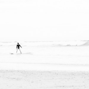 Surfeuse sereine terminant sa glisse au bord de l'eau, capturée en noir et blanc, incarnant un moment de plénitude et de connexion avec l'océan.