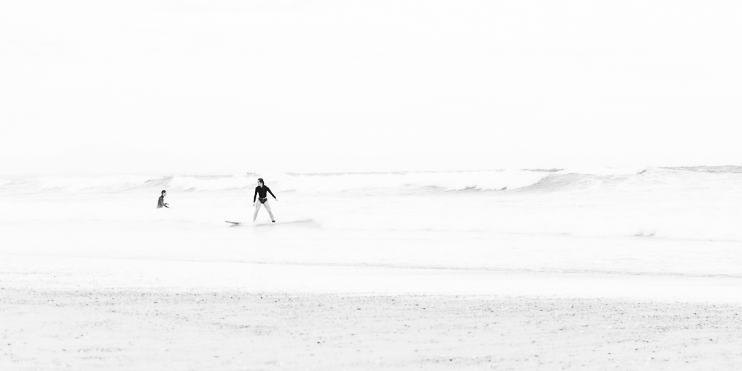 Surfeuse sereine terminant sa glisse au bord de l'eau, capturée en noir et blanc, incarnant un moment de plénitude et de connexion avec l'océan.