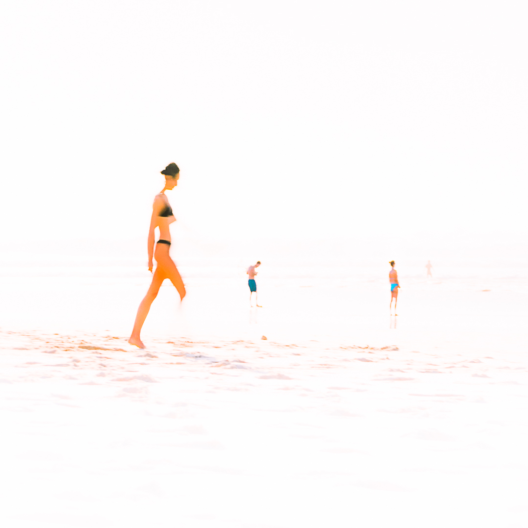 Silhouette floue d'une femme en maillot de bain sur une plage lumineuse, capturée avec une technique de flou de mouvement, évoquant la douceur et la fluidité d'une aquarelle poétique.