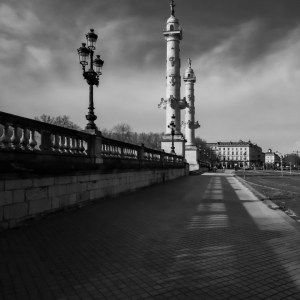Photographie d'art graphique en noir et blanc des colonnes rostrales de Bordeaux, place des Quinconces. La composition en ombre et lumière avec ligne de fuite dirige le spectateur vers ce monument historique.